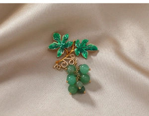 Macro detail of green grape cluster brooch with gold leaf on satin background