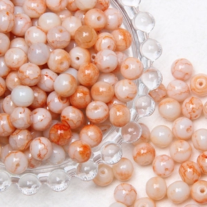 Macro detail of 8mm creamy white round glass beads with orange mesh pattern in glass bowl