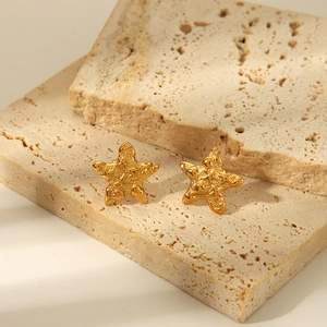 Détails de boucles d'oreilles étoile de mer dorées avec texture sur pierre beige