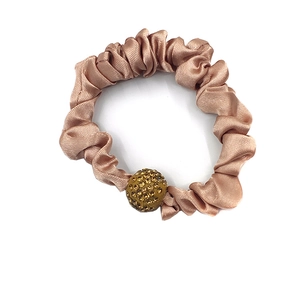 Detailed macro view of champagne satin scrunchie with a gold rhinestone ball ornament