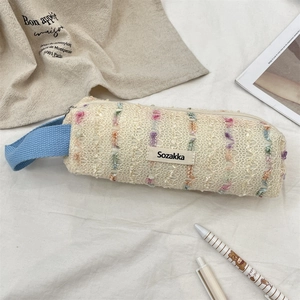 Close-up of floral knit pencil case with colorful pom-poms and a blue handle strap