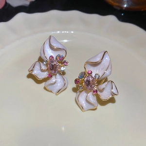 Macro view of flower stud earrings with white enamel petals and pink crystals in a ceramic dish