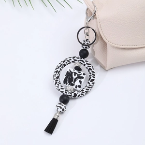 Detail view of a cow print silicone keychain featuring a cow tag, beads and black tassel