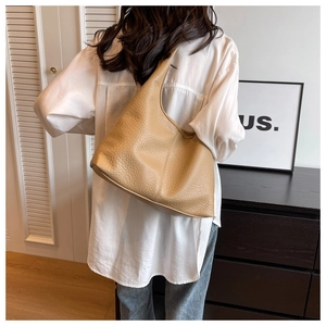 Litchi texture detail of large camel shoulder tote bag worn by a model in a modern room