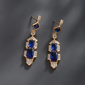 Close-up of gold dangle earrings with blue rectangular stones and micro-pave crystals