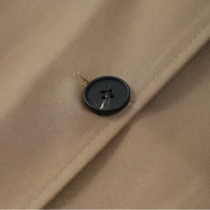 Makroaufnahme der khakifarbenen Twill-Struktur und des Marmorknopfes am Trenchcoat-Mantel