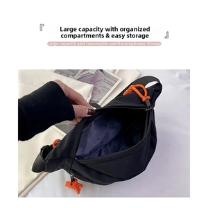 Detail view of black canvas crossbody bag with large interior storage and orange zipper pull
