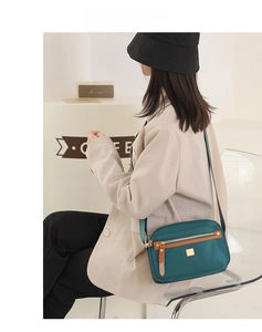 Detail of dark green nylon crossbody bag featuring leather trim and gold-tone hardware