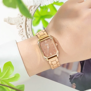 Dettaglio di un orologio rettangolare in oro rosa con quadrante in legno al polso di donna