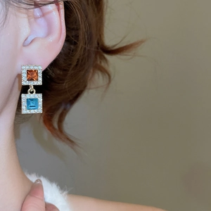 Détail de boucles d'oreilles carrées géométriques avec cristaux orange et bleus brillants