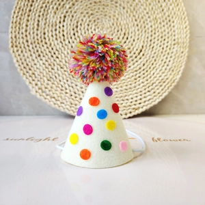 Polka dot pet party hat with colorful pom-poms and elastic strap on a clean white surface