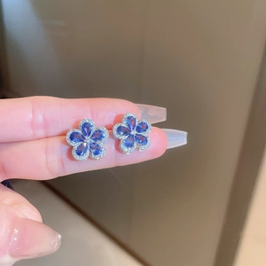 Close-up of blue zircon flower earrings with silver micro-pave crystals on finger