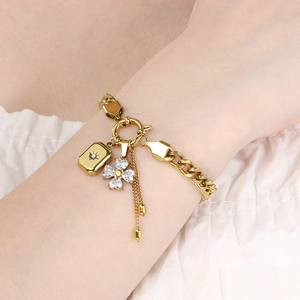 Close-up of gold stainless steel chain bracelet with star and flower charms on wrist