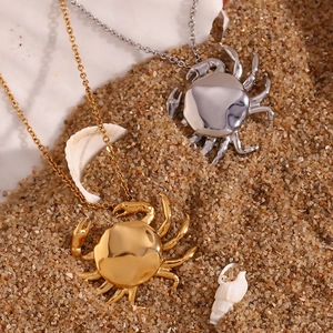 Close-up of gold and silver crab necklaces on a beach with shells and sand background