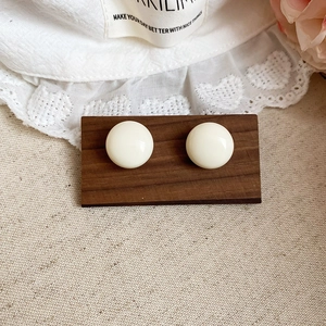 Close-up of elegant creamy white dome stud earrings on vintage wooden display card
