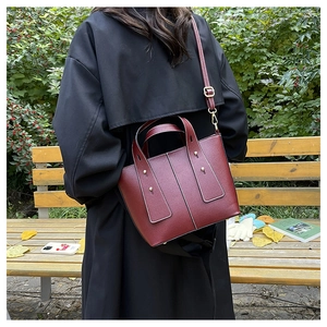 Détail du sac seau bordeaux avec texture litchi et rivets dorés sur un banc de parc public