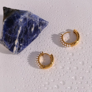 Detail of 18K gold-plated hoop earrings with small white pearls on a white wavy background