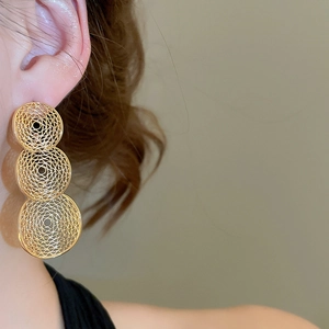 Close-up of a model wearing gold hollow triple circular earrings with pleated metal texture