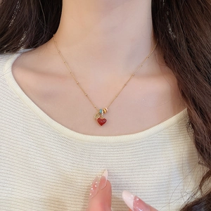 Close-up of 18k gold heart necklace with red pendant and colorful enamel rings on model