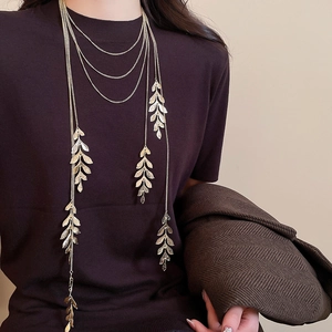 Detail of layered gold leaf pendant necklace on a model showing elegant textured tassels