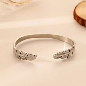 Close-up of silver stainless steel cuff bracelet with detailed feather ends on a warm base