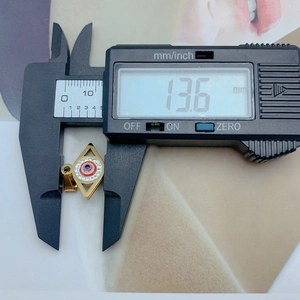 Detailed measurement of golden evil eye pendant showing 13.6 mm width on digital caliper