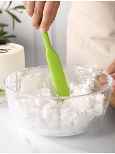 Small green silicone spatula mixing ingredients in a glass bowl for baking