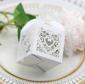 Close-up of white laser-cut heart favor box with organza ribbon on a decorative plate