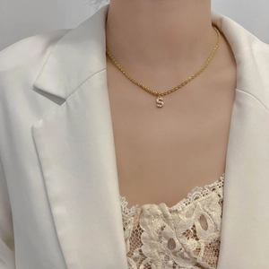 Détail d'un collier chaîne torsadée en acier titane doré avec un pendentif lettre S