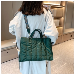 Detailed view of a green quilted nylon tote bag with patterned strap on a model back