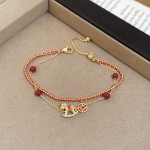 Close-up of double-layer gold bracelet with red beads and a zircon horse pendant