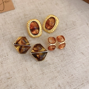 Detail showing amber resin stud earrings with gold plating on beige fabric