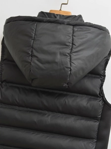Detail of black hooded puffer vest showing glossy nylon fabric and horizontal quilting