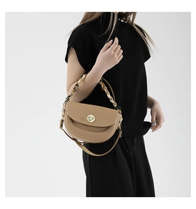 Detail of camel leather saddle bag featuring a gold twist lock and marble chain strap