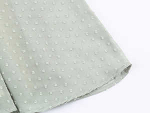 Détail du tissu en mousseline vert clair avec texture à pois 3D et coutures de précision