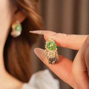Close-up of vintage gold earrings with green gems and white pearls on ear