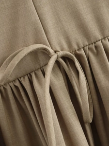 Detailed macro shot of the brown waist tie and pleated texture on a linen sleeveless dress