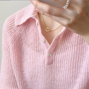 Close-up of a heart pendant necklace in silver and gold mix worn on a pink knit shirt