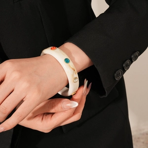 Detail of a creamy marble acrylic cuff bracelet with colorful inlaid crystals and gold rim