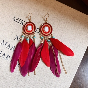 Detail of vintage flower enamel earrings with colorful feathers and golden metal tassels