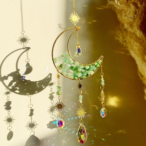 Detail of moon suncatcher with green crystals casting rainbow light on a beige wall