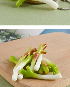 Detail of realistic artificial green onion pendant with keychain ring on wood board