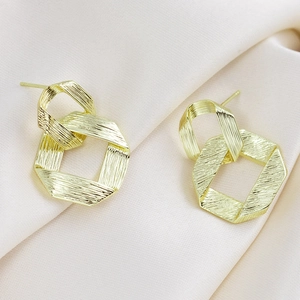 Detalle de pendientes geométricos dorados con acabado de metal cepillado sobre seda