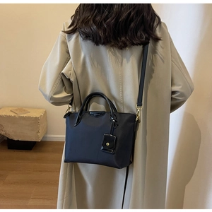 Detailed view of black nylon tote bag with CLEAN logo worn over a beige coat