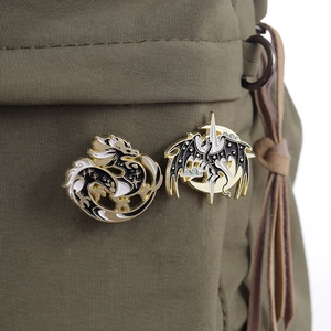 Detailed close-up of dragon enamel pins in black and white on a green canvas bag