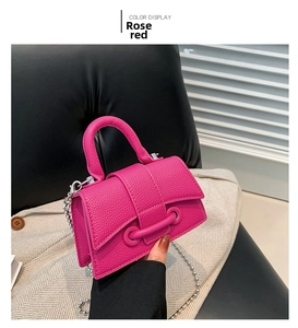 Detail of rose red mini handbag with litchi grain texture and silver chain strap