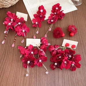 Close-up of red fabric flower earrings with crystal tassels and pearls on a wood surface