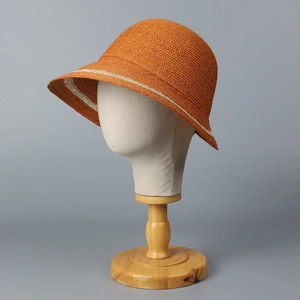 Detail of orange raffia sun hat showing woven texture and decorative white ribbon band
