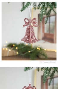 Pink glitter Christmas bow bell ornament hanging on a festive tree with warm lights