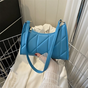 Sky blue quilted baguette bag with gold zipper held against a white blazer